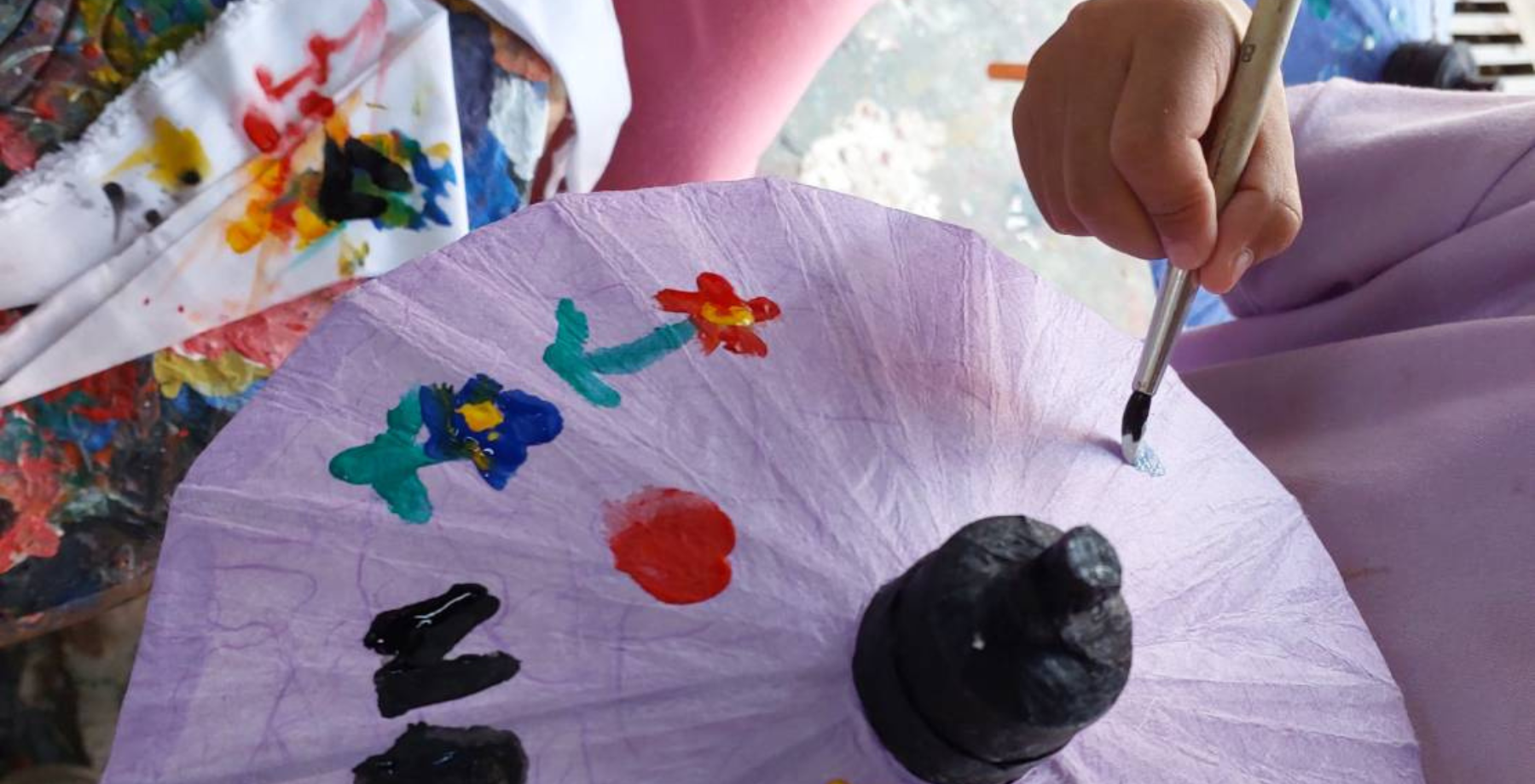 Close up of a child's hand painting on a traditional umbrella on a Buy A Trip, Give A Trip