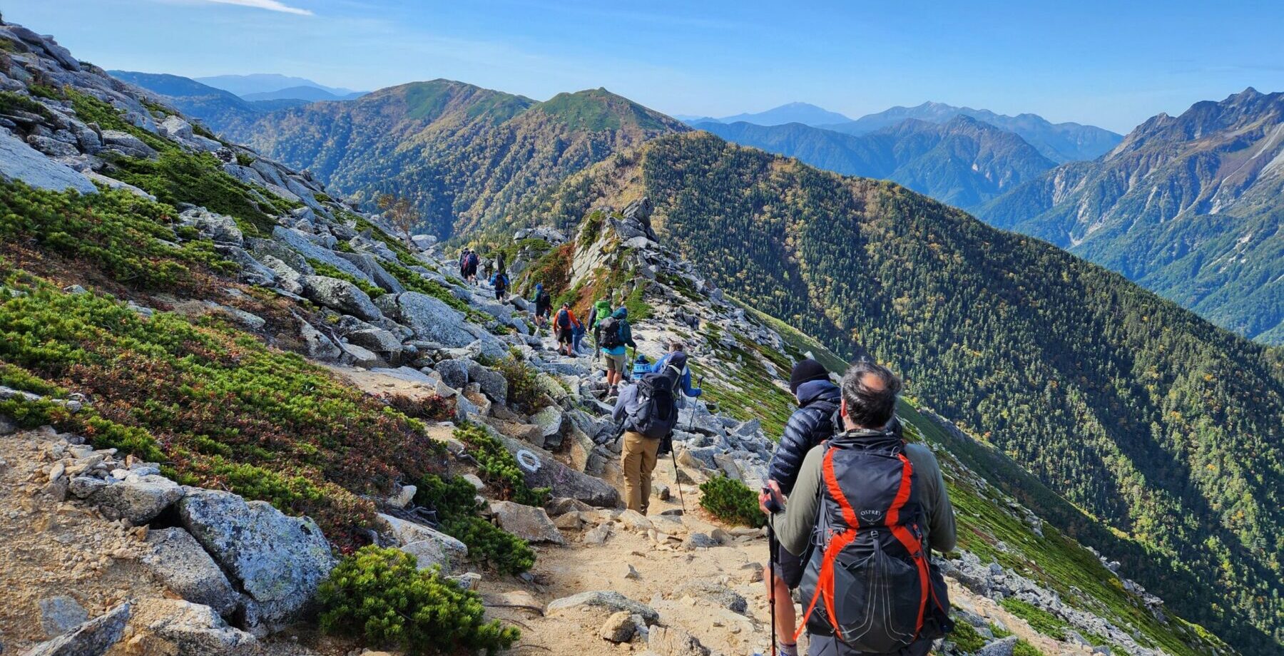 charity challenge group hiking through mountains wearing backpacks and carrying hiking poles.