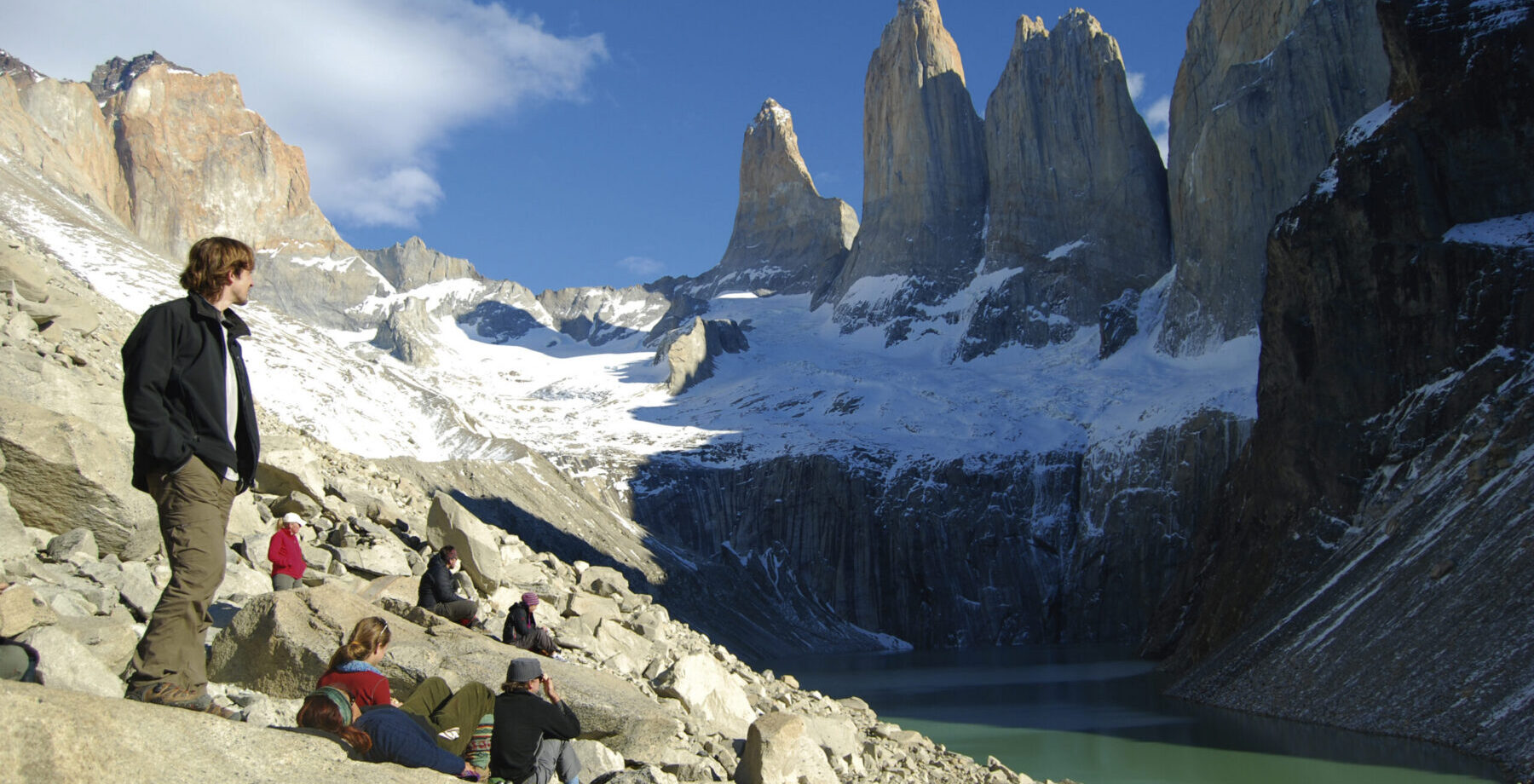 person surrounded by mountains standing by turquoise waters in Patagonia during a charity challenge