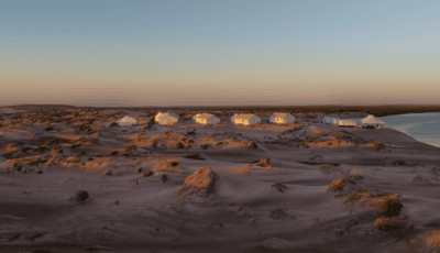 tents for a group donor trip itinerary amidst an isolated sandy beach beside the ocean at sunset.