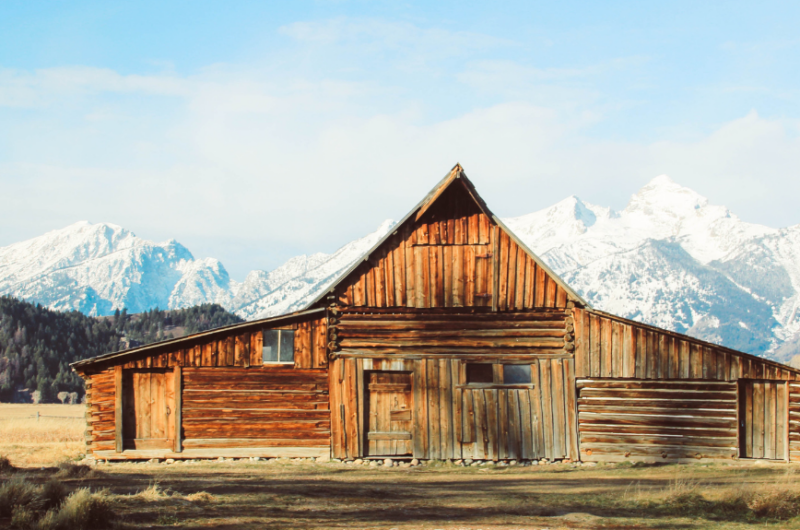 log cabin used for nature based company retreat surrounded in open field with forest and snow-capped mountains in the background