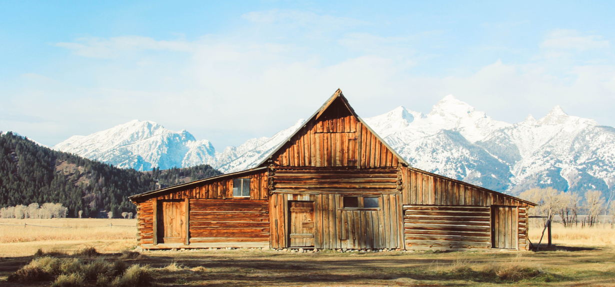 log cabin used for nature based company retreat surrounded in open field with forest and snow-capped mountains in the background
